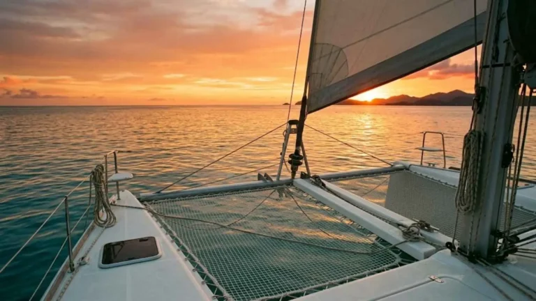 Wide catamaran deck at golden hour during a Caribbean sunset sailing cruise excursion, with open ocean horizon and warm light reflecting off calm water