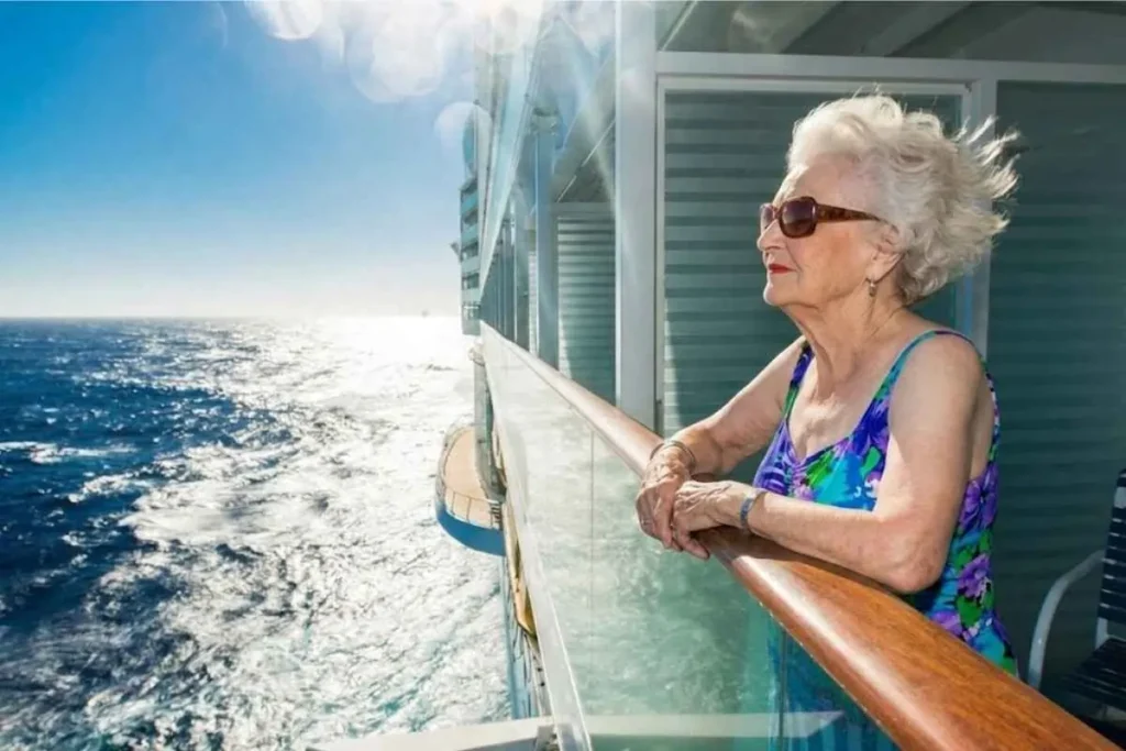 Woman on cruise ship balcony gazing at the ocean — one of the best ways to get a balcony room without a single supplement cruise surcharge is via repositioning sailings